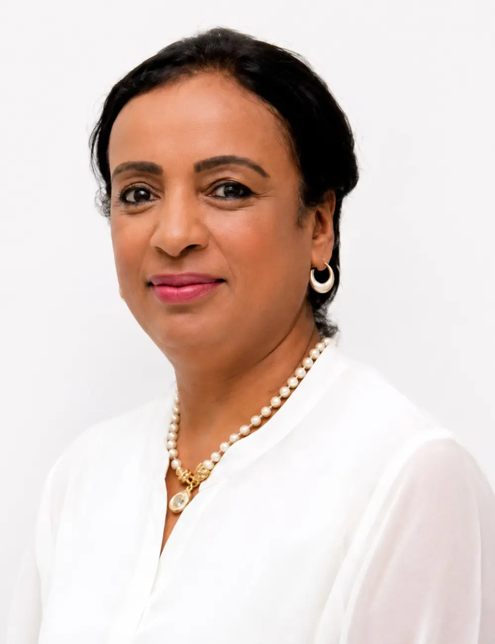 Professional portrait of a smiling woman with short dark hair, wearing a white blouse and pearl necklace against a light background.