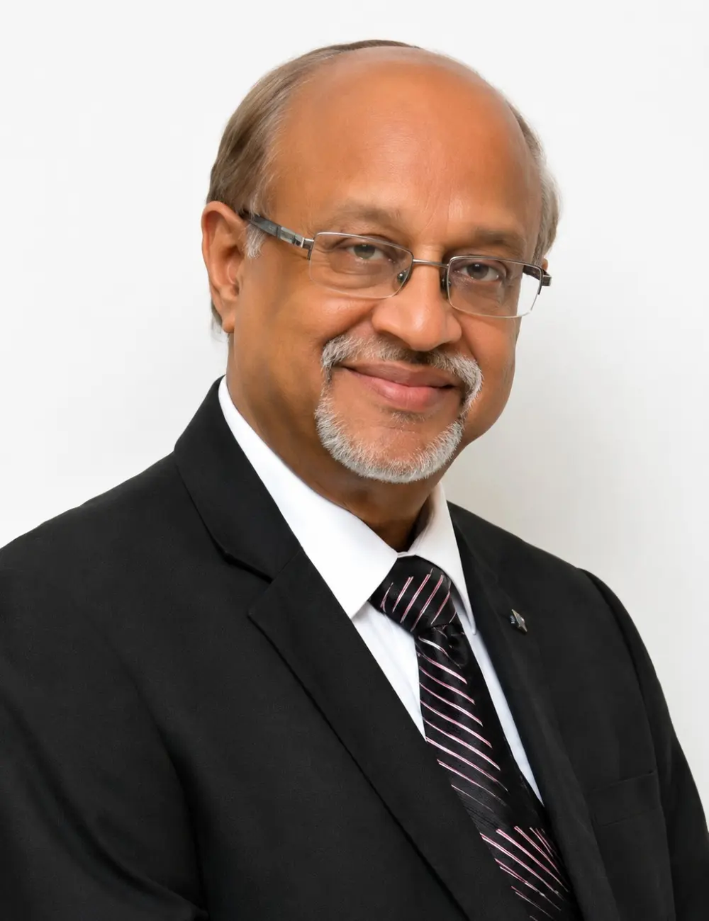 Portrait of a smiling mature man in a black suit, white shirt, and striped tie, wearing glasses against a white background.