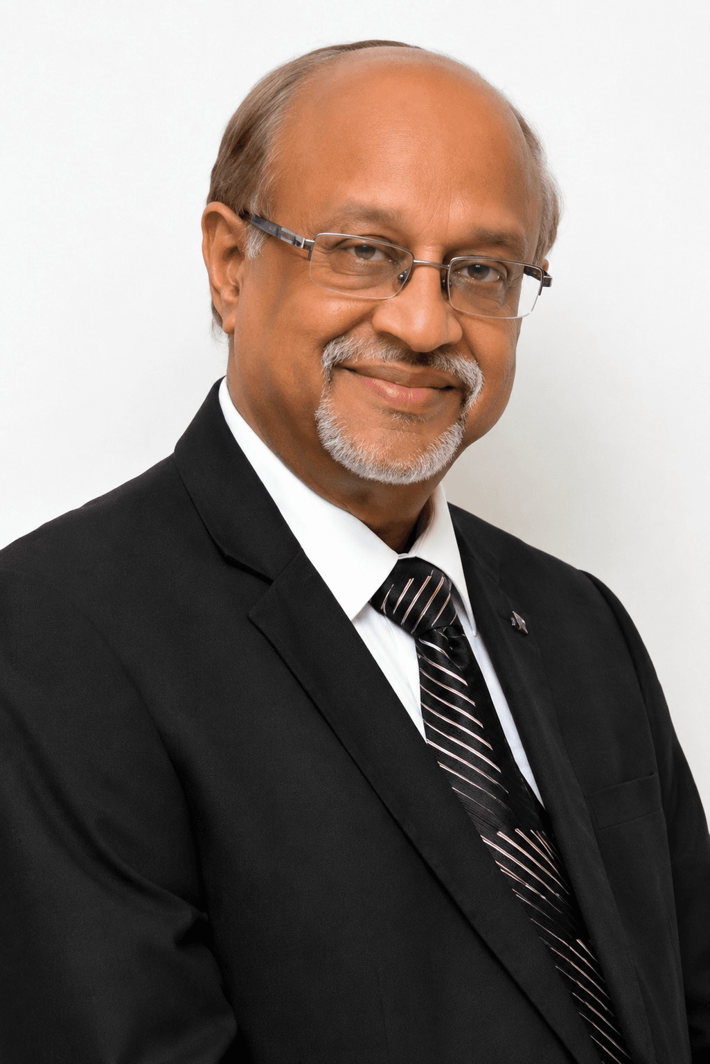 image - Saraogi Hospital Smiling older man in a black suit, white shirt, and striped tie; wearing glasses for a professional portrait.